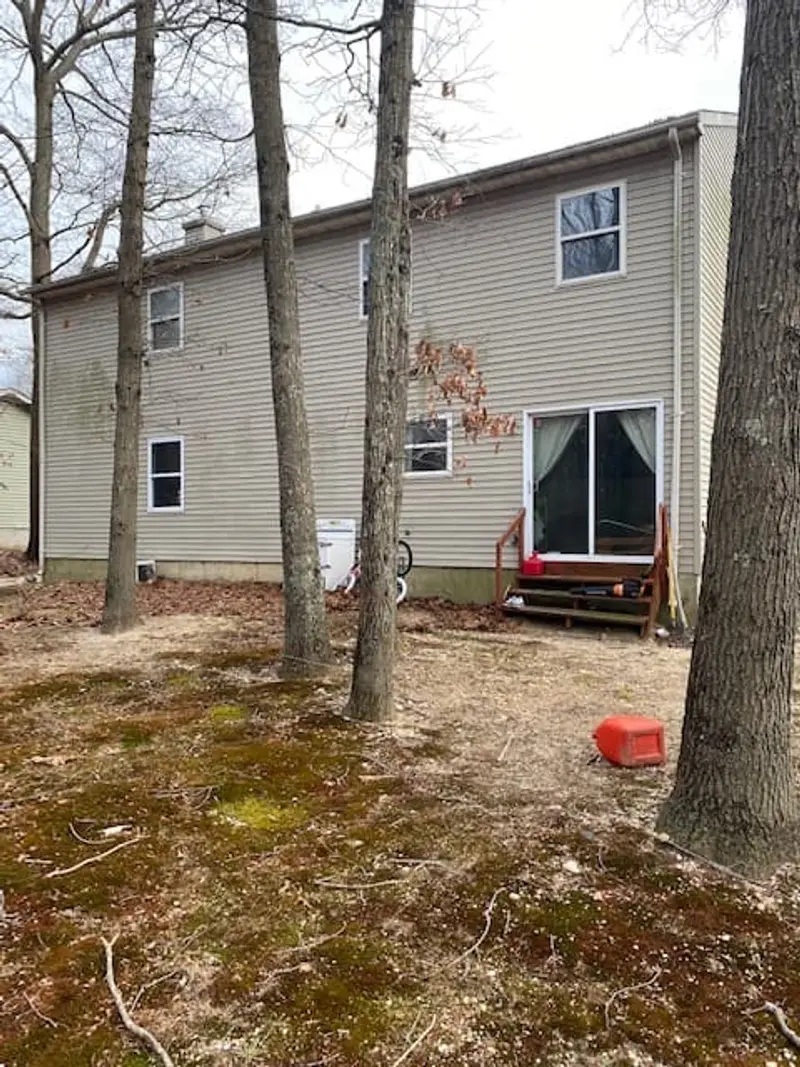 Back of a two-story house among bare trees, Middle Island, NY